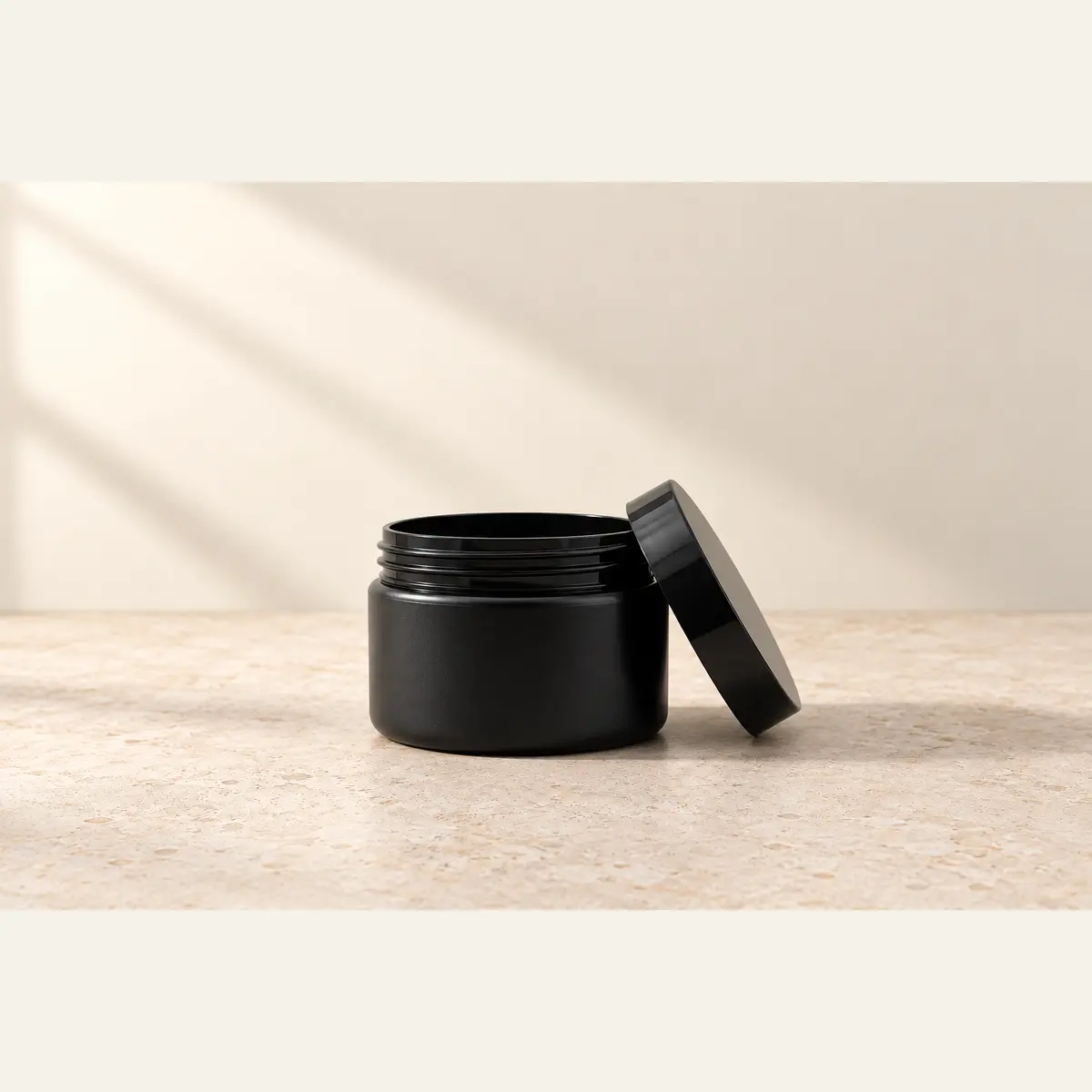 Black 125 g Cosmetic Jar · Black Lid photographed on a warm neutral studio background
