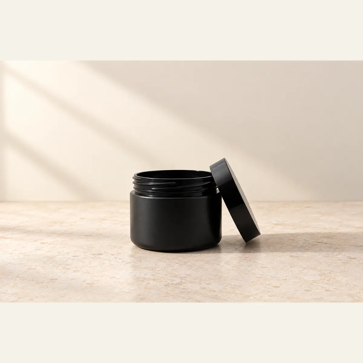 Black 50 g Cosmetic Jar · Black Lid photographed on a warm neutral studio background